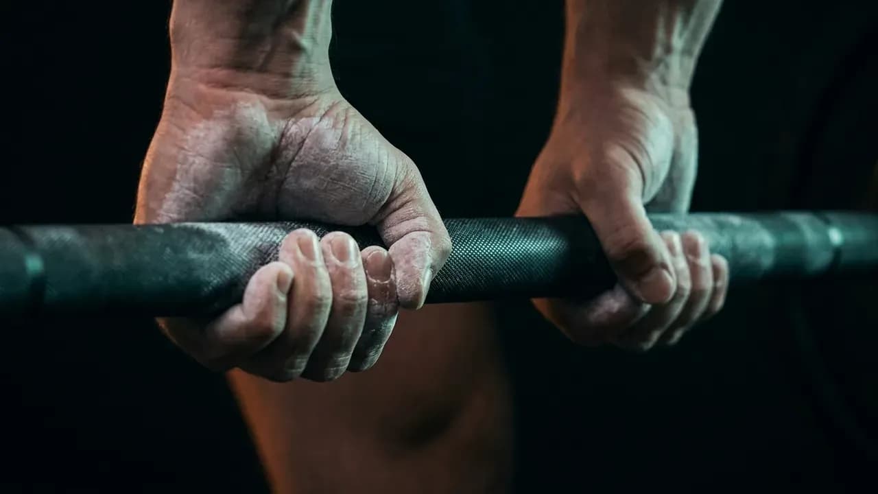 a close-up view of chalked hands gripping an iron barbell knurling before a heavy deadlift attempt